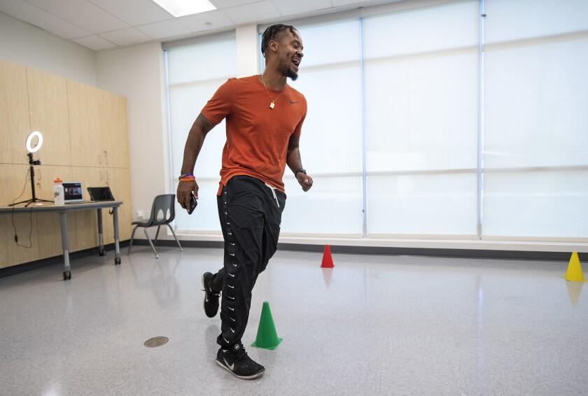 Physical education teacher Alfredo Crossman-Chávez Jr. jogs around cones in a classroom while teaching a lesson about cardiovascular endurance. He told his online students to follow along by setting up a similar course at home to jog or walk around in a timed manner.(Mel Melcon / Los Angeles Times)